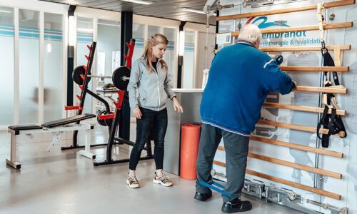 Fysiotherapeut Manon helpt Coen bij verschillende oefeningen in de oefenzaal fysiotherapie voor ouderen en 65 plus