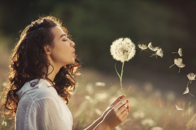 Vrouw heeft geen burn-out meer en blaast paardenbloemen weg in een veld
