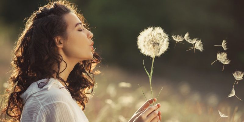Vrouw heeft geen burn-out meer en blaast paardenbloemen weg in een veld