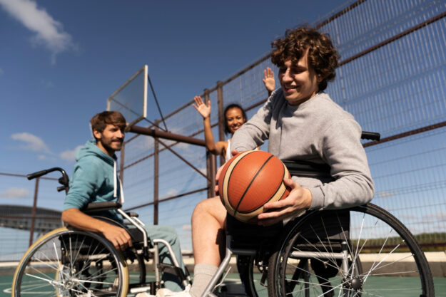 Twee mensen met MS zitten in een rolstoel en spelen basketbal