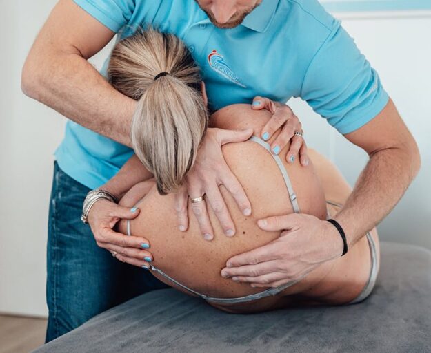 Manuele therapie Lienden Manueel therapeut in een blauwe polo helpt een patiënt zonder shirt door middel van manuele therapie in Lienden bij chronische lage rugklachten en door de rug gaan.